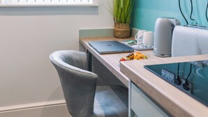 A modern office space with a wooden desk, a laptop, a grey chair, a potted plant, and a white coffee machine.