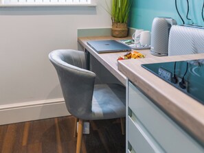 A modern office space with a wooden desk, a laptop, a grey chair, a potted plant, and a white coffee machine.