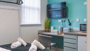 A hotel room with a bed, a desk, a television, and a small kitchenette.