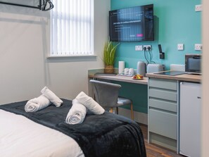 Ein Hotelzimmer mit Bett, Schreibtisch, Fernseher und einer kleinen Küchenzeile.
