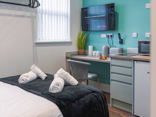 A hotel room with a bed, a desk, a television, and a small kitchenette.