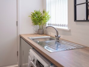 A kitchen with a stainless steel sink, a potted plant, and a window with blinds. - Hilltop Apartment 5 - UK50597 (Earl Shilton)