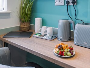 Et tekøkken med en bærbar computer, kaffemaskine, brødrister og en tallerken med frugt.