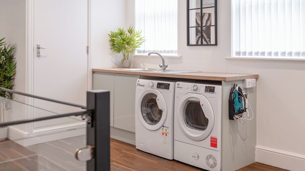 A laundry area with two front-loading washing machines, a sink, and a potted plant.