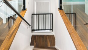 A staircase with wooden steps and black railings, leading to a landing with a white door and a window with blinds.