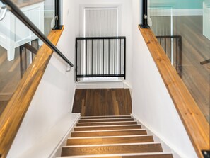 Eine Treppe mit Holzboden und schwarzen Geländern, die zu einer Zwischenebene mit einer weißen Tür und einem Fenster mit Rollläden führt.