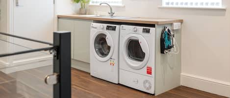 A laundry room with two front-loading washing machines, a sink, and a potted plant.