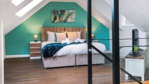A bedroom with a sloped ceiling, a bed with a wooden headboard, a teal accent wall, and a painting above the bed.