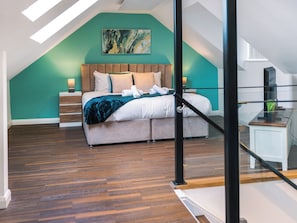 Un dormitorio con techo inclinado, cama con cabecero de madera, pared de acento color turquesa y un cuadro sobre la cama.