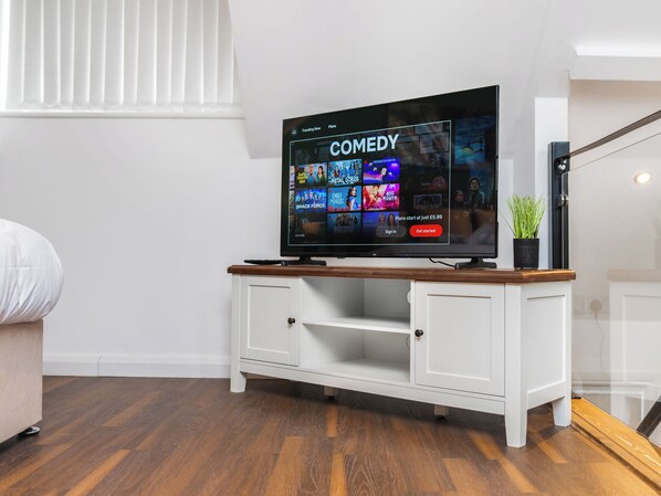 Un televisor de pantalla plana sobre un mueble blanco con tapa de madera, mostrando la interfaz de un canal de comedia.