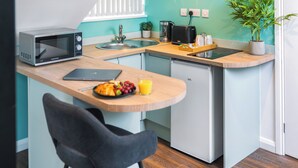A compact kitchen with a microwave, toaster, and sink. There's a small dining area with a chair and a table set with a croissant, grapes, and orange juice.