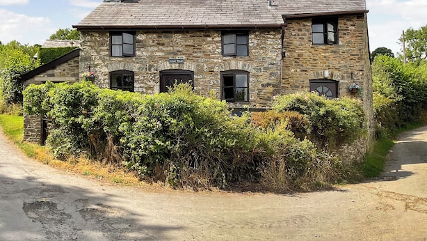 A stone house with a gabled roof, multiple windows, and a chimney.