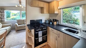 A compact kitchen with wooden cabinets, a gas stove, and a window offering a view of greenery. - 2 bedroom accommodation in Machynlleth (Machynlleth)