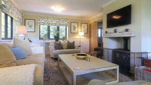 A cozy living room with a fireplace, comfortable seating, and a television mounted on the wall. - 4 bedroom accommodation in Royal Wootton Bassett (Royal Wootton Bassett)