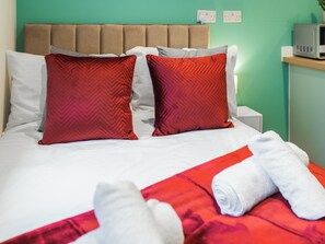 Una cama con dos almohadas rojas, una blanca y una colcha roja. Hay una toalla blanca sobre la cama.
