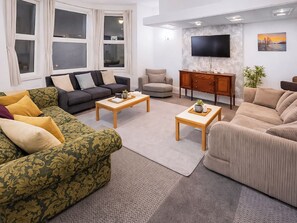 Ein Wohnzimmer mit einer Couch, einem Sessel, einem Couchtisch, einem Fernseher und einem Schrank.