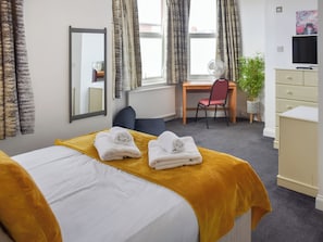 Ein Hotelzimmer mit einem Bett, einem Schreibtisch, einem Stuhl, einem Fernseher und einer Pflanze.