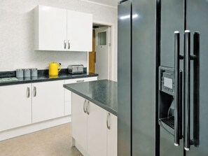 A modern kitchen with white cabinets, a black refrigerator, and a yellow kettle on the counter.