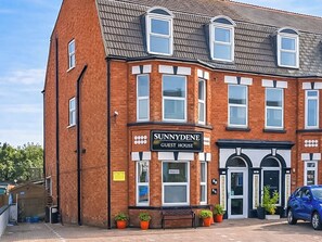 Ein Backsteinhaus mit einem Schild, auf dem 'SUNNYDENE GUEST HOUSE' steht.