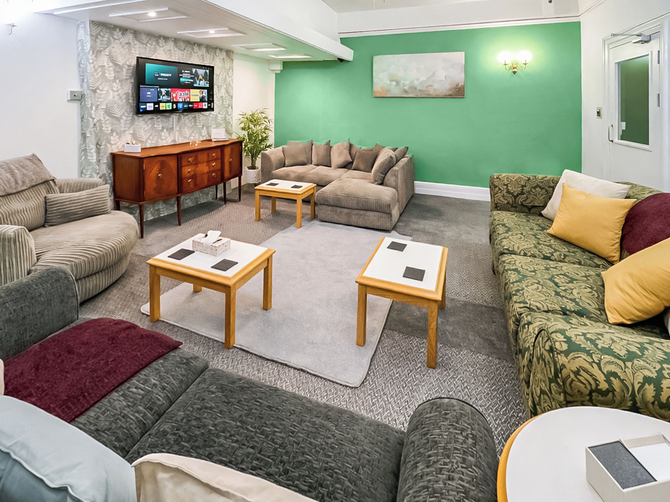 A living room with a sofa, two coffee tables, a TV, and a green accent wall.