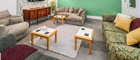 A living room with a sofa, two coffee tables, a TV, and a green accent wall.
