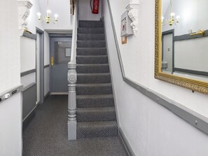 A staircase with a textured carpet, a white wall with a gold-framed mirror, and a fire extinguisher on the wall.