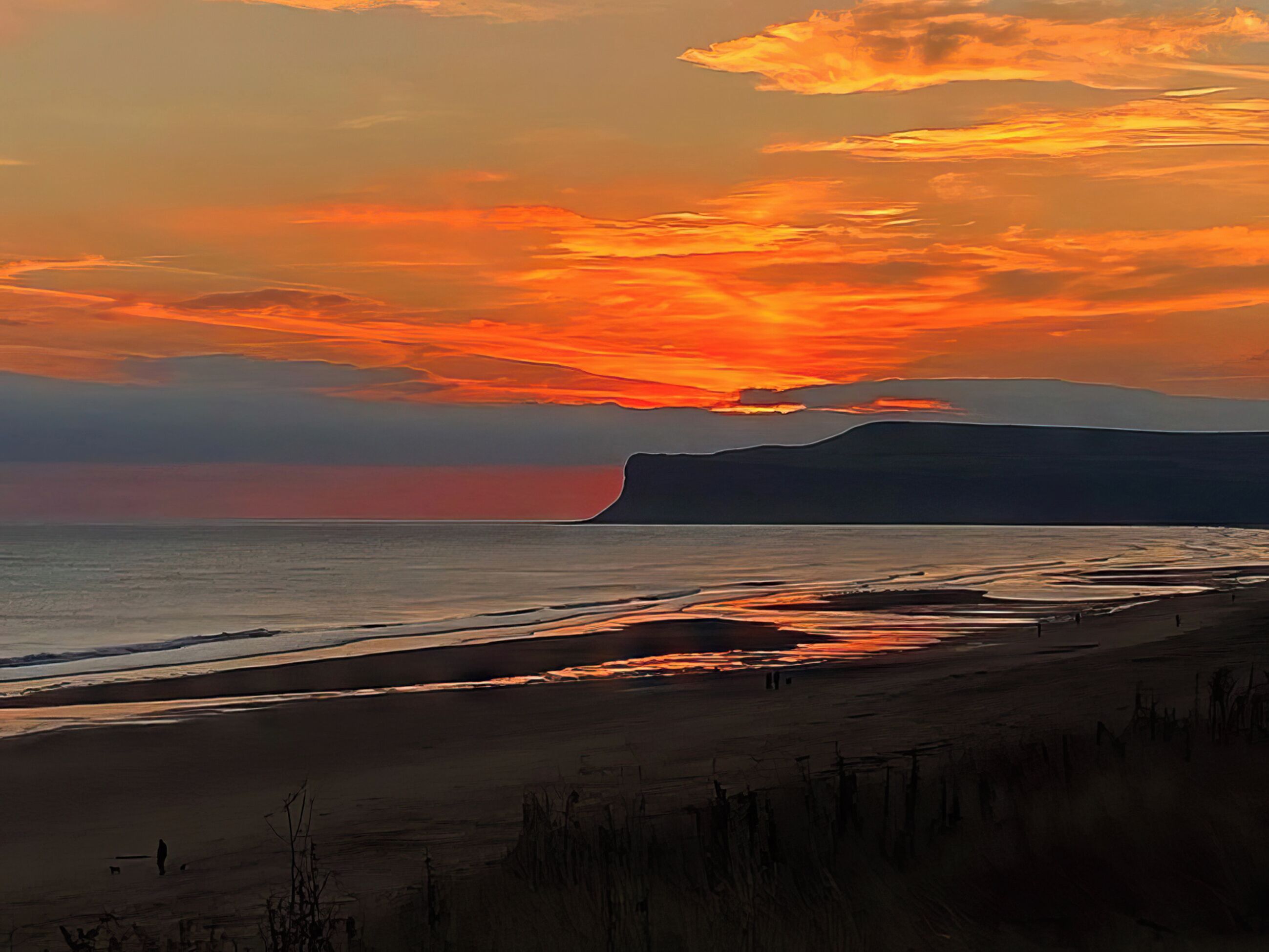A beach with a sunset, waves, and a distant mountain.