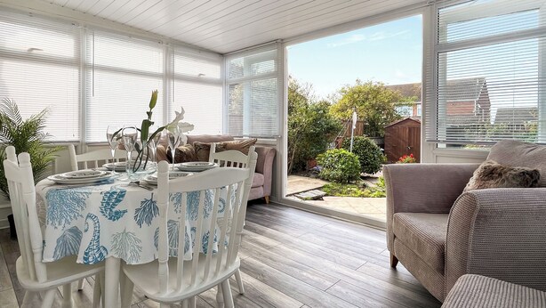 A dining area with a table set for four, surrounded by white chairs, and a view of a garden through large windows. - 2 bedroom accommodation in Redcar (Redcar)
