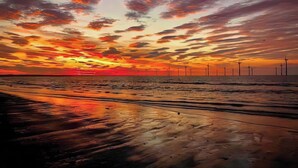 A beach with a sunset, calm sea, and wind turbines in the distance. - 2 bedroom accommodation in Redcar (Redcar)