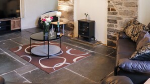 Una sala de estar con chimenea de piedra, un sofá, un televisor y una mesita con un florero y vasos.