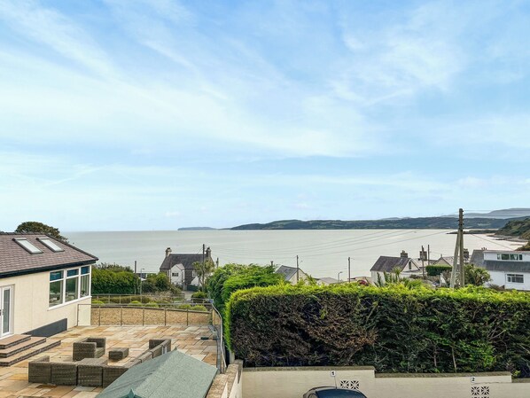 Zona residencial con vista al mar, un patio empedrado con mobiliario y un seto.