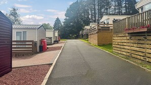 A row of mobile homes with a paved driveway, wooden fences, and a clear sky.