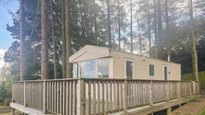 A single-story wooden cabin with a deck, surrounded by tall trees.