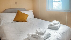 A neatly made bed with white linens and a single mustard-colored pillow. There are folded white towels on the bed.