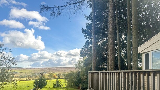 A wooden deck with a view of a green field and distant hills.