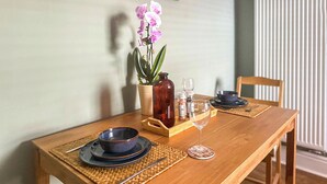A wooden dining table set with plates, bowls, cutlery, a glass, and a vase with flowers.