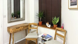 A corner workspace with a wooden desk, two chairs, a small table, and potted plants.