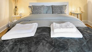 A neatly made bed with a dark quilted bedspread and two folded white towels.