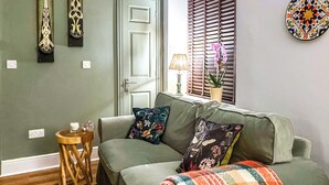 A cozy living room with a green sofa, floral cushions, a plaid throw blanket, and a small wooden side table.