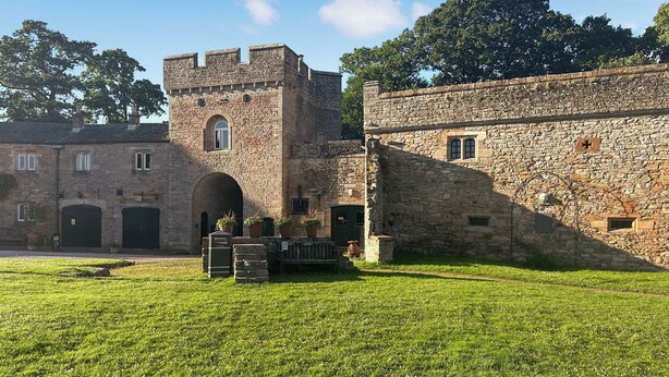 A stone building with a tower, arched entrance, and a grassy courtyard.
