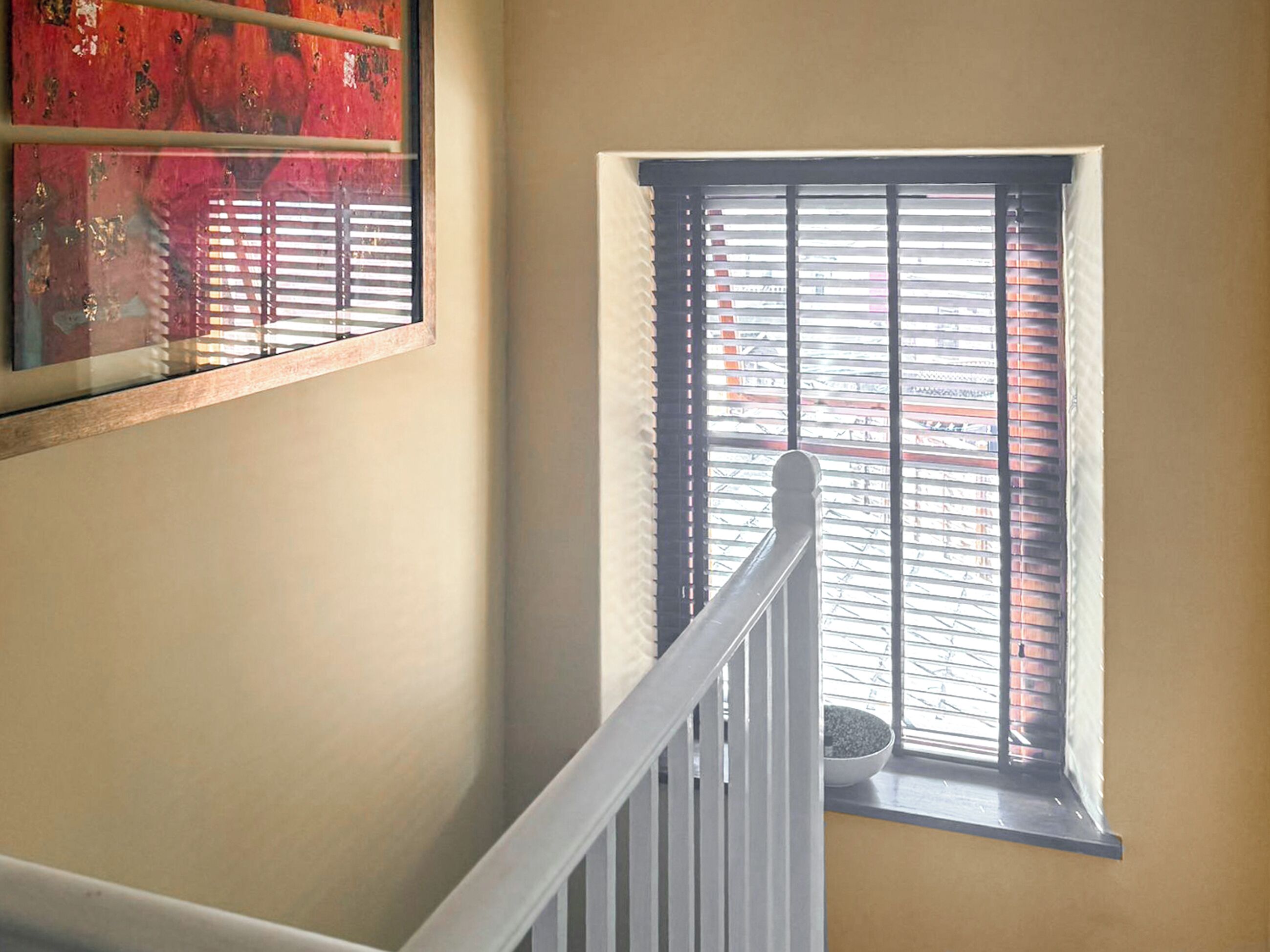 A staircase with a white railing leading to a window with black blinds.