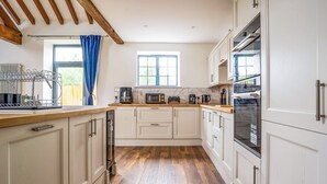 A modern kitchen with wooden flooring, white cabinets, a built-in oven, and a window with blue curtains.