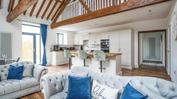 A spacious living room with a high ceiling, a kitchen area, and a staircase leading to an upper level.