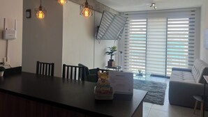 Ein modernes Wohnzimmer mit großem Fenster, einer Couch, einem Couchtisch und einem Essbereich mit Stühlen und einer Kücheninsel.