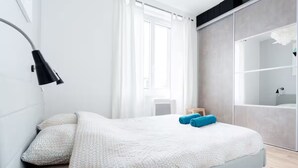 A modern bedroom with a bed, a nightstand, a lamp, a wardrobe, and a window with curtains.