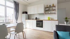 A modern kitchen with white cabinets, a black oven, and a wooden countertop. There is a dining table with chairs and a view of the city through large windows.