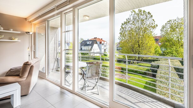 Un salon moderne doté d’une grande porte-fenêtre coulissante donnant sur un balcon avec une rambarde en métal et une vue sur le quartier.