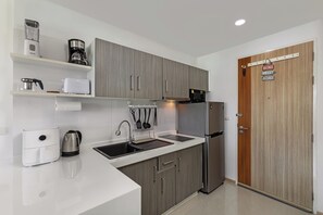 A modern kitchen with grey cabinets, a white countertop, a stainless steel refrigerator, a coffee maker, a toaster, and a kettle. - Studio in Ozone Condo in Kata A702 (Karon)