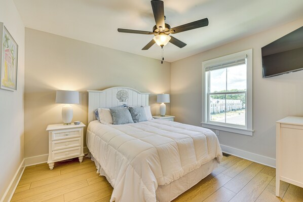 Une chambre à coucher comprenant un lit, des tables de chevet, un ventilateur de plafond, une fenêtre avec vue et un téléviseur à écran plat.