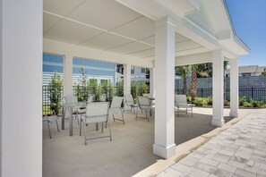 Ein Patio im Freien mit weißen Säulen, Metallstühlen und einem Glastisch.